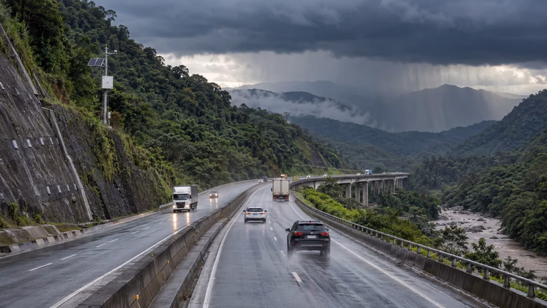 Rodovia concedida em região de serra sob tempestade, com estruturas de contenção e monitoramento do risco climático.